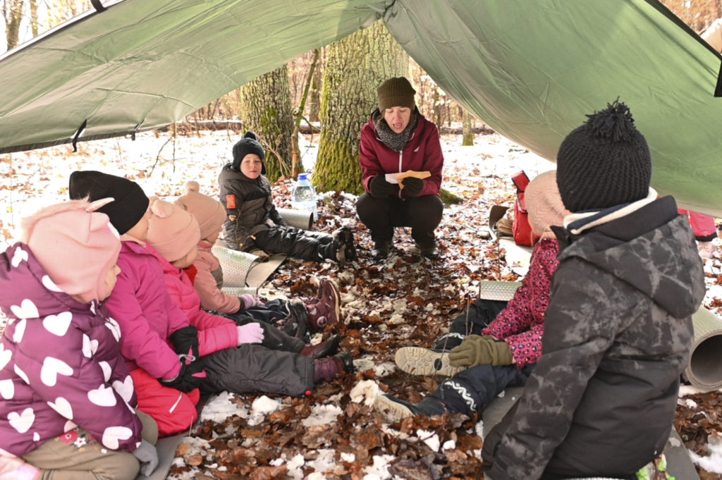 Dzieci siedzą pod daszkiem w lesie.