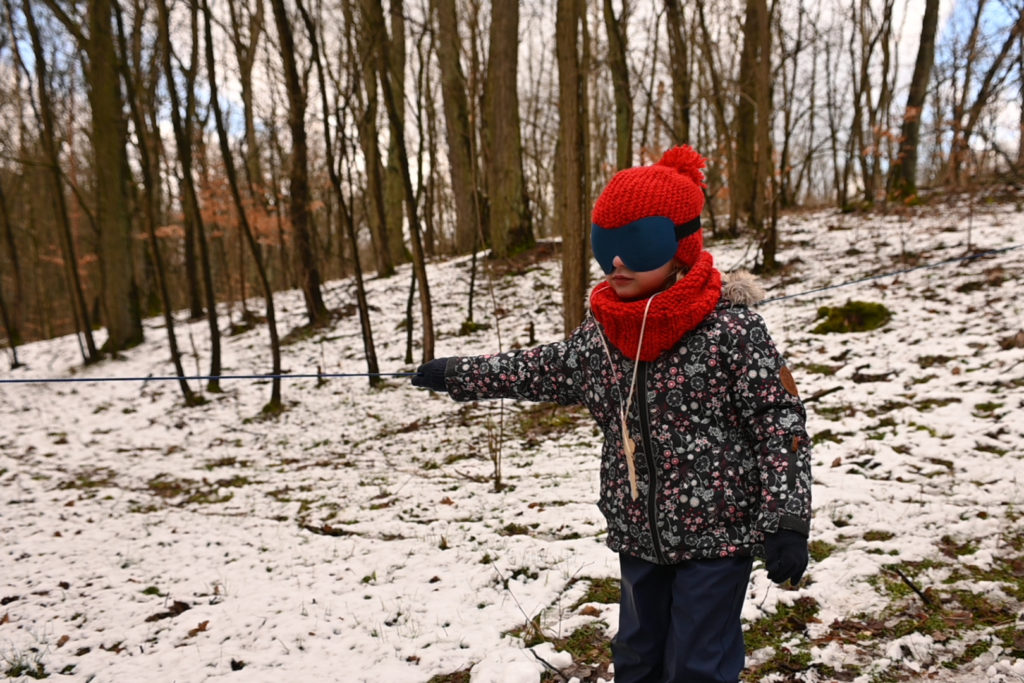 Dziewczyna z zasłoniętymi oczami idzie przez las.